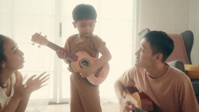 音乐时刻:亚洲父母和孩子在家里享受吉他游戏时光。