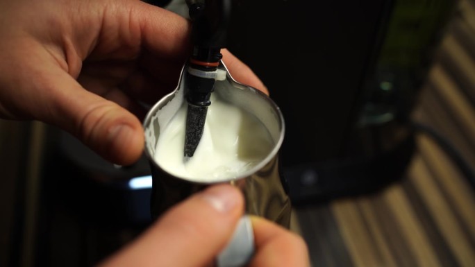 一个男人用咖啡机的管子在壶里搅牛奶