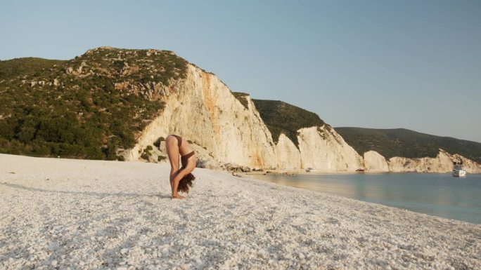美丽成熟的女人在沙滩上向太阳瑜伽致敬。这个片段是系列的三分之一