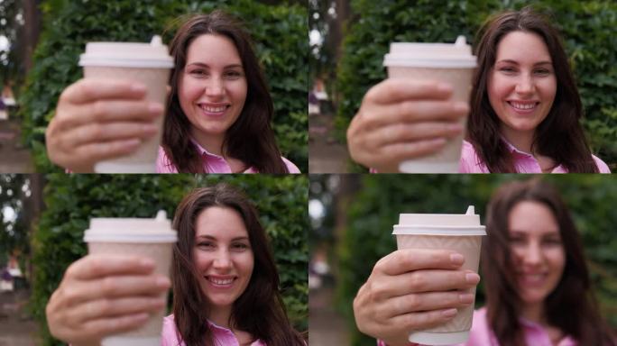 特写:一个年轻迷人的女人面带微笑，端着一杯咖啡来到镜头前，背景是一道草篱。她的头发在风中飘动