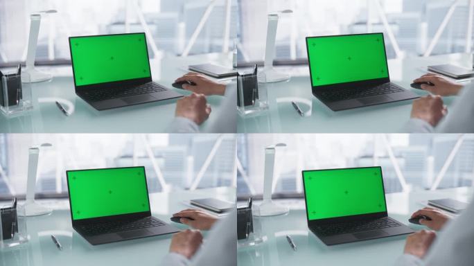 在肩膀上的镜头与公司员工使用笔记本电脑模拟绿屏Chromakey显示器。一个人坐在桌子后面，用无线鼠