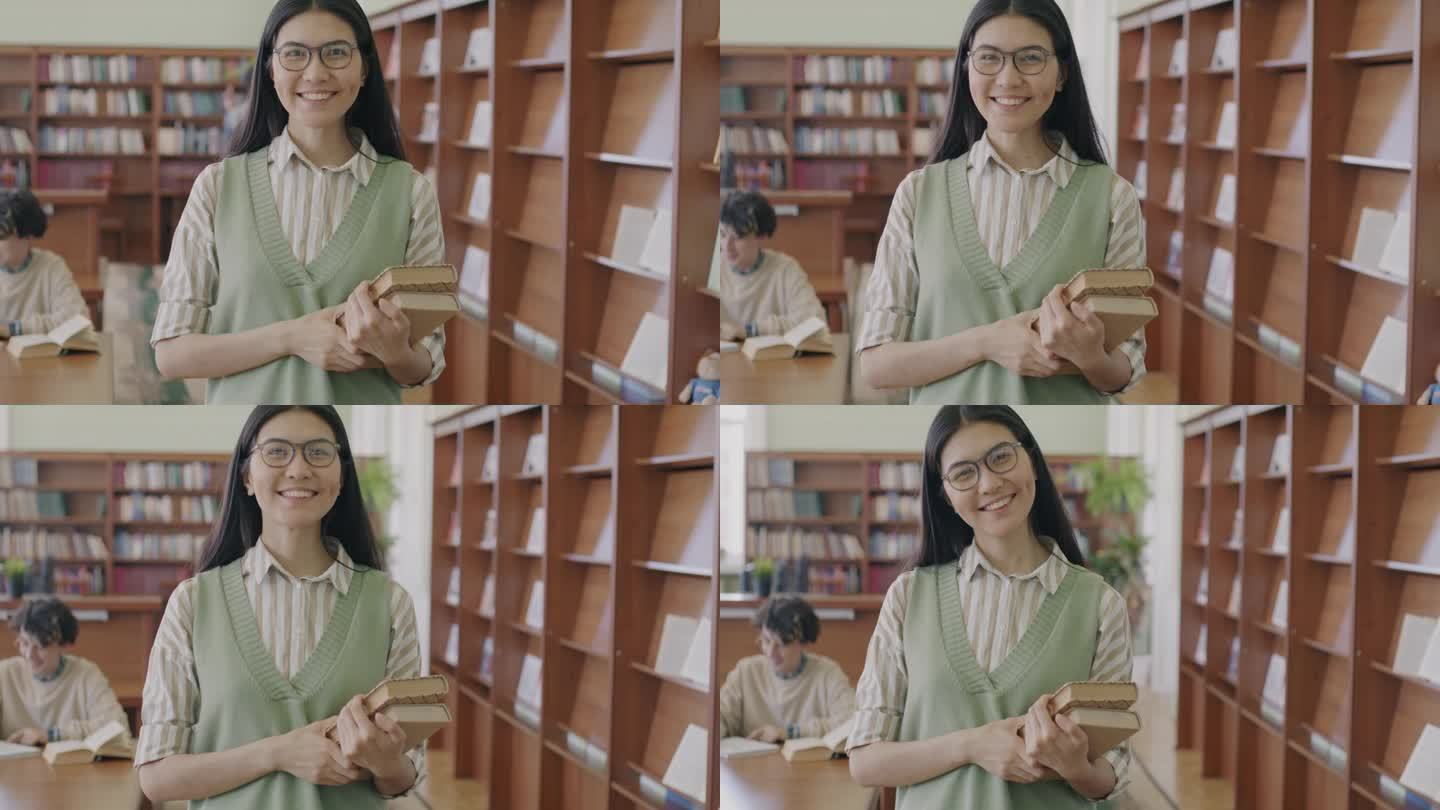 聪明的亚洲女学生站在图书馆大厅拿着书微笑的慢动作肖像