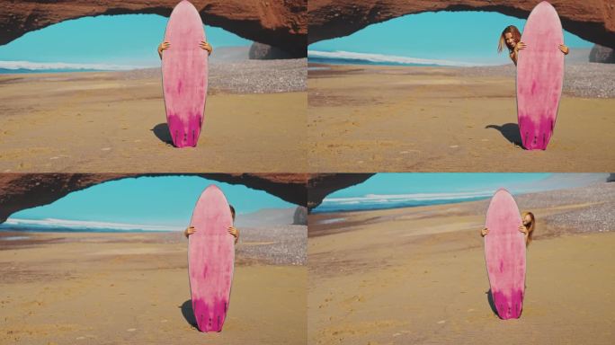 一名身穿休闲装的年轻女子在海边的一个粉色冲浪板后面摆姿势拍照，她走到冲浪板后面