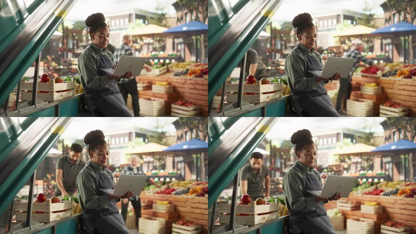 多民族非洲女商人在手提电脑上工作，为城市广场上的国际美食节做准备。一位女士坐在有机农产品摊位旁