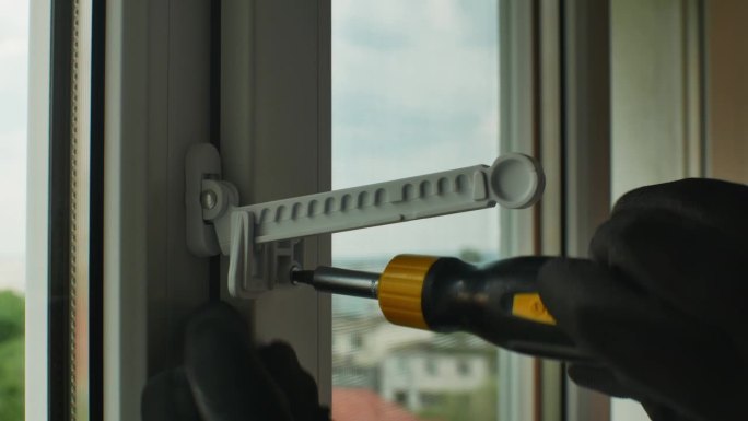 公用螺丝刀拧紧塑料开窗限位器固定螺钉带手套的手特写用螺丝刀拧紧窗限位器固定螺钉到塑料窗框上。回家修理