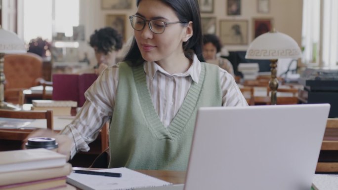 亚洲女生用笔记本电脑打字，用智能手机在大学图书馆学习