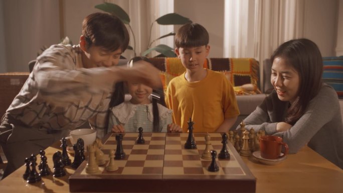 一个幸福的韩国家庭在家里的客厅里共度时光。聪明的小男孩试图在一场国际象棋比赛中战胜支持他的爸爸、妈妈