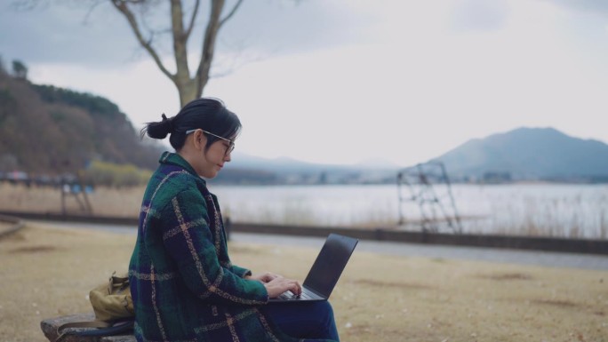 一名年轻的女性自由职业者游客在旅行期间住的酒店的湖边使用笔记本电脑。