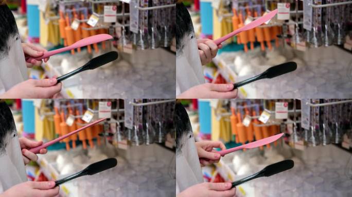 年轻女子正在选择不同的硅胶刮刀(特写)。购买厨房用品