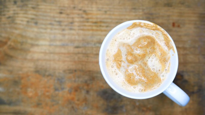 一个热气腾腾的咖啡杯，俯视图:一个人把沸水倒在一杯奶油咖啡上。用勺子搅拌咖啡。桌上有一杯咖啡。工作台