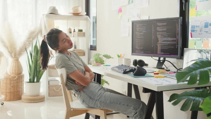年轻的亚洲女孩开发程序员工作过度，在电脑旁的桌子上睡着了，在家里办公室的电脑上上传编码程序数据库。工