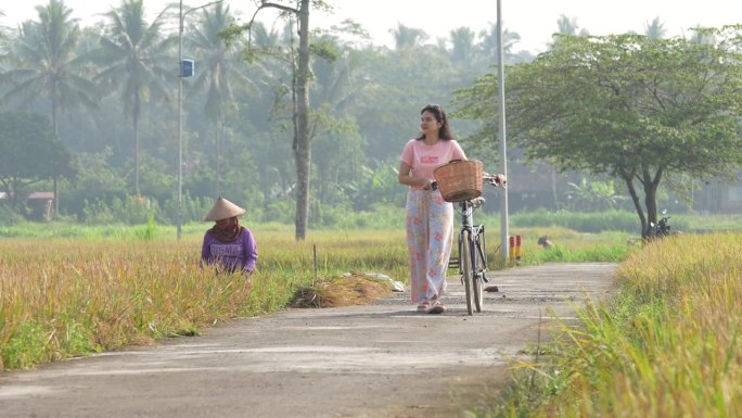 在村子里骑自行车，在农民收割水稻的背景下开心吗