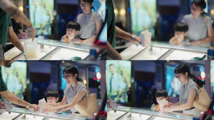 美丽的亚洲母亲和她的儿子等着电影院的工作人员为他们舀爆米花。