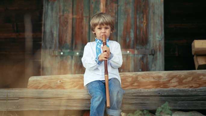 小男孩在演奏木管木笛——乌克兰索皮卡。民间音乐概念。乐器。小孩穿着传统的刺绣衬衫-维希亚万卡。孩子坐