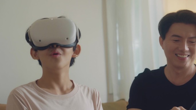 亚洲男人使用笔记本电脑，亚洲男孩戴着虚拟现实眼镜，头戴式耳机，坐在家里开始玩电子游戏。