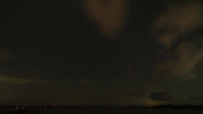 海湾星空的夜间延时拍摄，左下方是码头，头顶上飘着小云