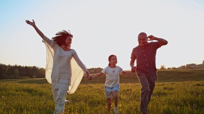 夕阳西下，一对夫妇和他们的女儿在草地上欢笑奔跑
