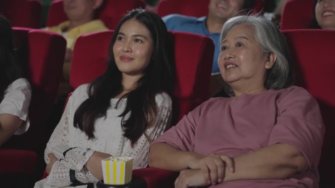 一群快乐的人在电影院看电影。微笑的亚洲母女坐在电影院的座位上看电影。娱乐的概念