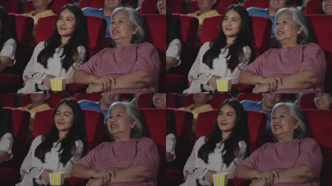 一群快乐的人在电影院看电影。微笑的亚洲母女坐在电影院的座位上看电影。娱乐的概念