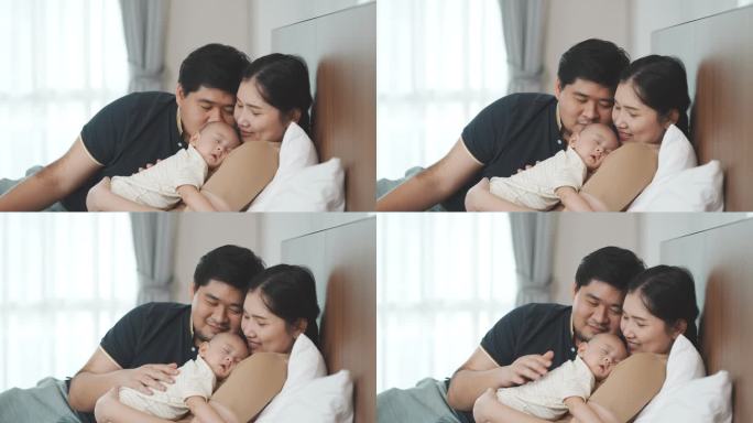 一对亚洲父母抱着刚出生的儿子，哄他在家里的卧室里睡觉。母亲和孩子之间的关系