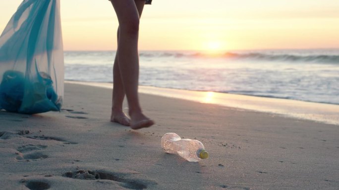 人，腿和塑料在海滩上回收，环保，停止污染或户外废物。志愿者在海边散步，在日落时捡起瓶子，在大自然中健