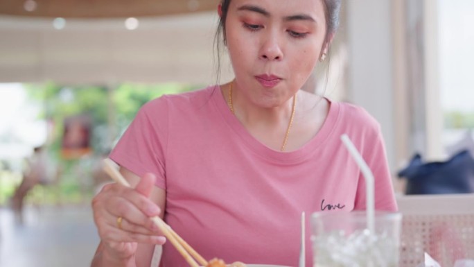 亚洲妇女在餐馆用筷子在碗里吃面条的特写。