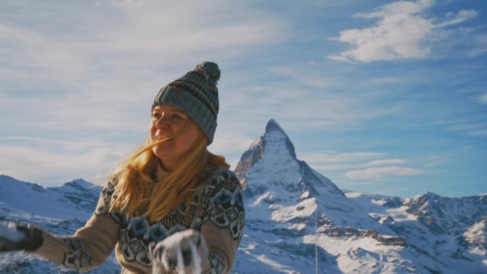 一个女人在山坡上向空中抛雪，背景是马特洪峰
