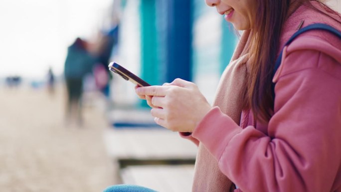 妇女用手机发短信和照片享受放松在布莱顿海滩五颜六色的房子