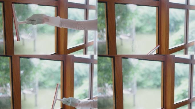 年轻的亚洲女人穿着围裙，在房子里擦窗户。有吸引力的成熟的管家清洁工喷洒酒精和擦拭凌乱肮脏的玻璃窗为家
