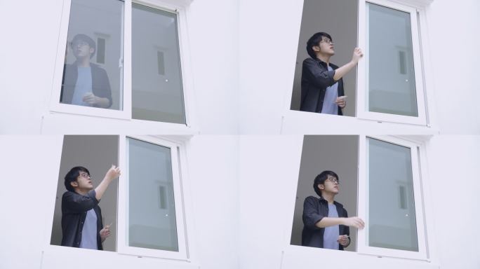 年轻的亚洲男子推开窗户，贴了一张贴纸，然后走开了