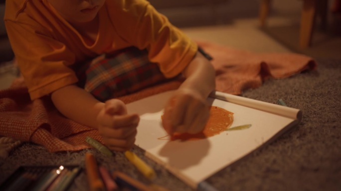可爱的韩国男孩躺在地板上，用铅笔和钢笔在笔记本上画画的特写。艺术儿童绘画和着色一个橙色水果在家里舒适
