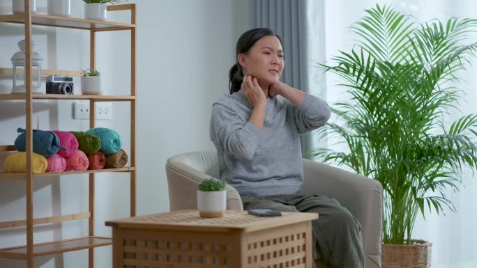 一位亚洲妇女坐在家里客厅的扶手椅上，皮肤痒得难受。
