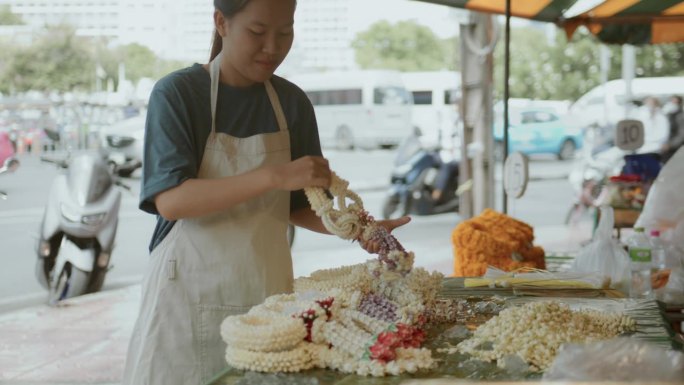 在曼谷的花卉市场，一位亚洲花店老板在她的店前摆上花环。