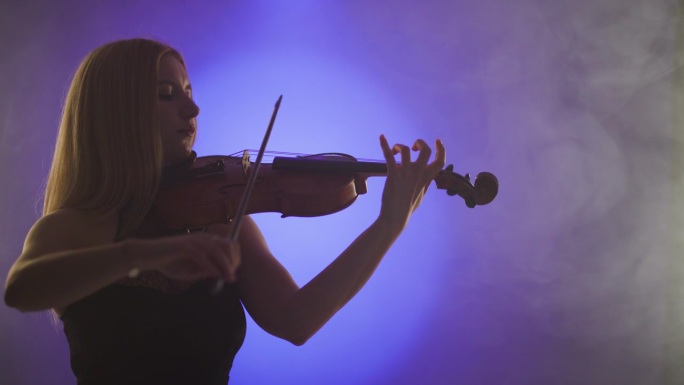 美丽的金发女子在蓝色和紫色的聚光灯下演奏小提琴，背景是烟雾。
