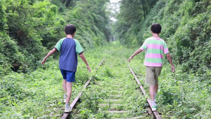 男孩走在铁轨上长满杂草的废旧铁轨两个小男