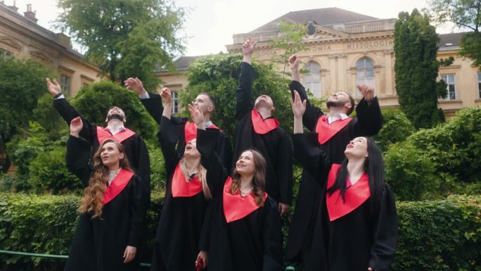 兴奋的学生，毕业生，高兴的扔毕业帽，在大学的花园里，他们都感觉很好