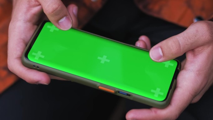 一名男子在户外玩游戏时双手拿着智能手机。用绿屏和铬键玩手机游戏模型