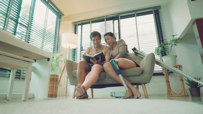 当亚洲残疾夫妇在沙发上看书时，自动清洁地板地毯的装置。智能家居科技，舒适生活