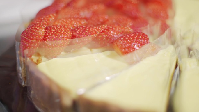 一个戴着黑色手套的厨师的手在草莓奶酪派上把草莓片围成一个圈。装饰蛋糕。制作草莓芝士派甜点的过程