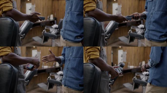 一名非洲裔美国男子在理发店用智能手机NFC技术完成信用卡支付后，理发师和顾客握手