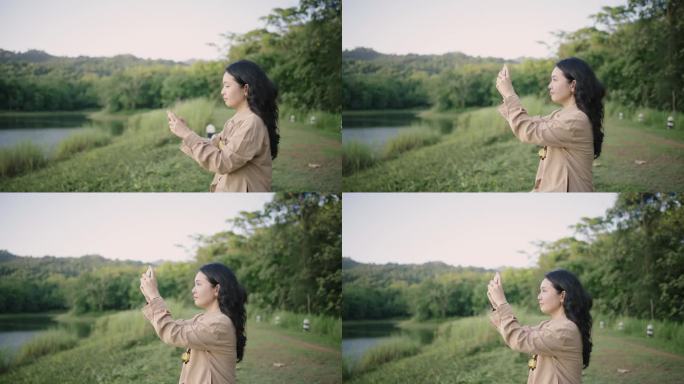 年轻的亚洲女子在大自然的河岸用智能手机拍摄令人惊叹的景色。她在欣赏美丽的景色。美丽的女孩深呼吸，