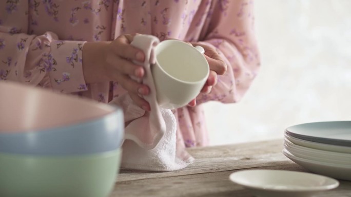 用茶巾擦杯子。年轻女子在家里打扫卫生时正在洗盘子。一堆干净的盘子