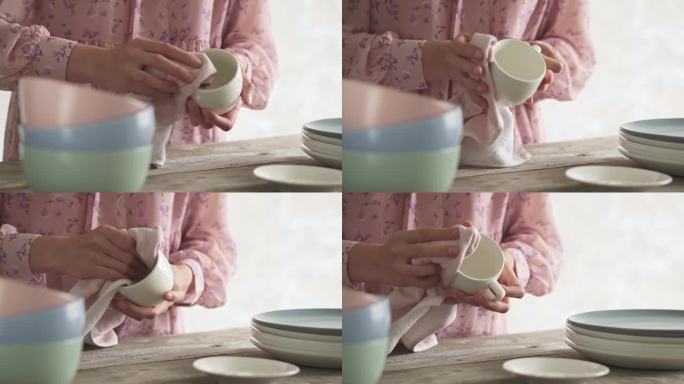 用茶巾擦杯子。年轻女子在家里打扫卫生时正在洗盘子。一堆干净的盘子