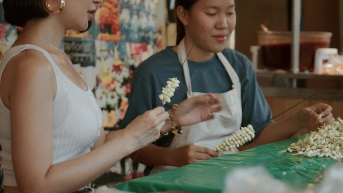 一位美丽的游客在曼谷向一位泰国花店老板学习如何制作花环。周末去泰国。