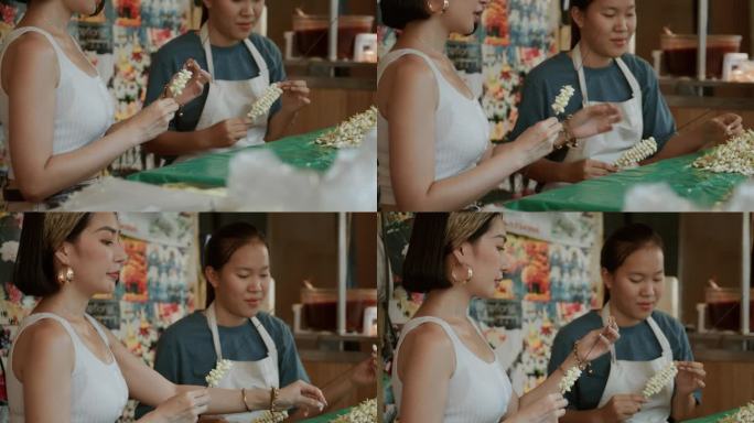 一位美丽的游客在曼谷向一位泰国花店老板学习如何制作花环。周末去泰国。