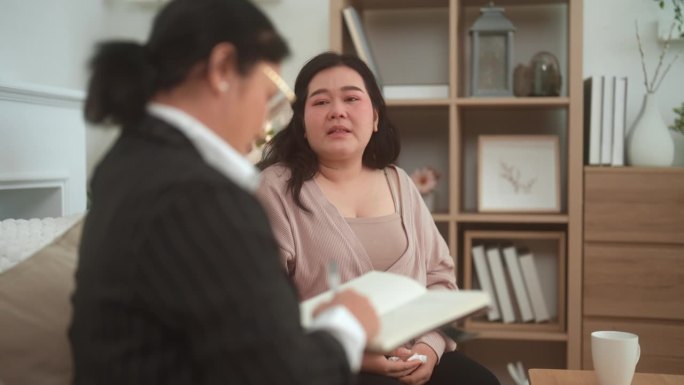 一名亚洲成年妇女在治疗过程中与她的肥胖病人交谈，跟踪她的症状。