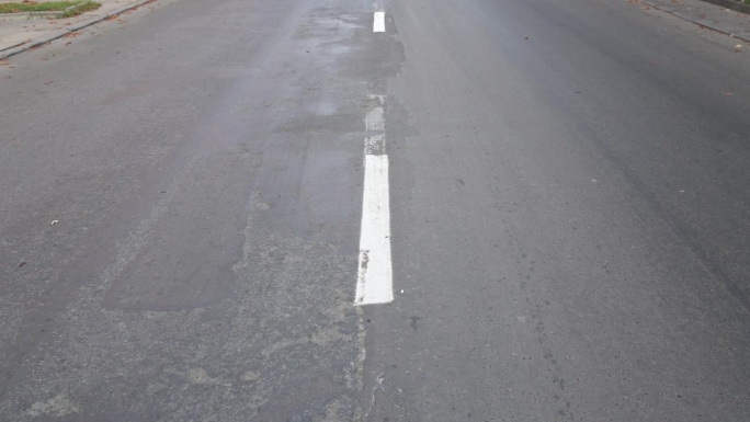 灰色的柏油路，中间有一条白色的条纹。用分割线详细说明老巷道按时间破损情况。路边有路边的落叶，为汽车让