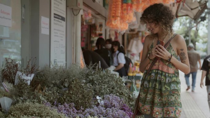 在曼谷的花卉市场，一位女游客在花店散步，与鲜花合影留念
