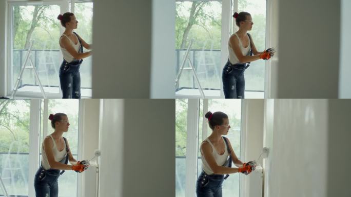 年轻女子用油漆滚筒刷着她梦想中的房子墙壁。穿防护服