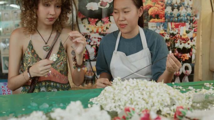 花店企业家亚洲妇女教一名女游客在她的店里自己制作花环。